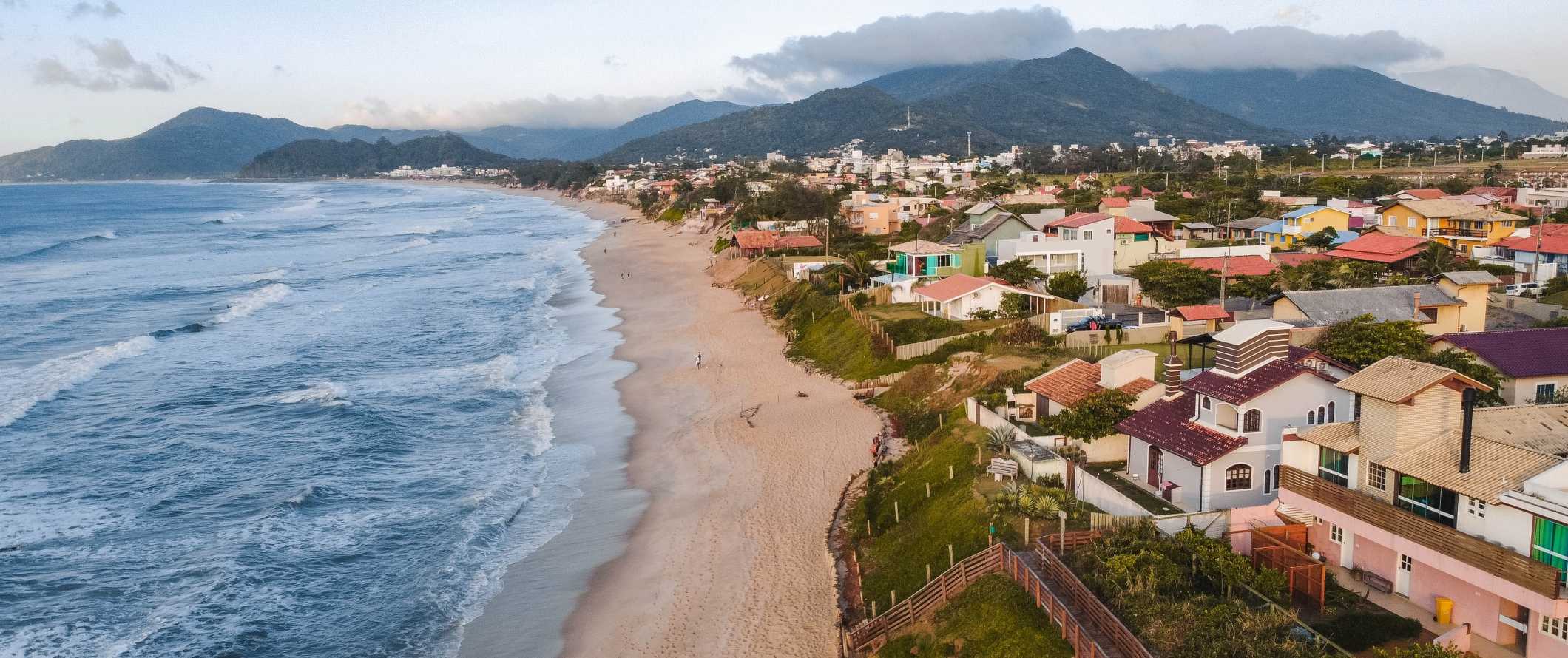 Casas mult i-coloridas ao longo da praia com montanhas em segundo plano em Florinopolis, Brasil