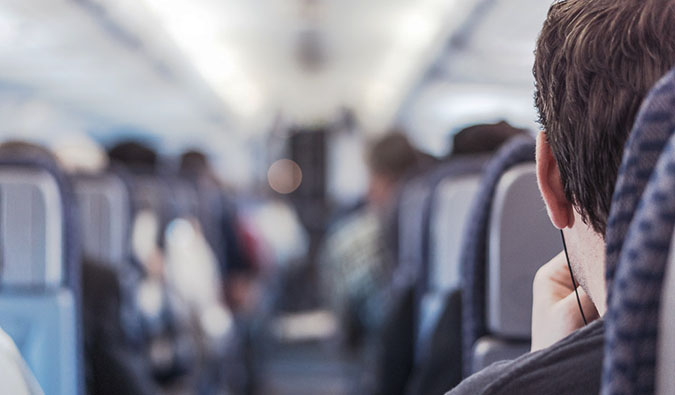 Um homem sentado em um avião olha para um comissário de bordo no corredor.