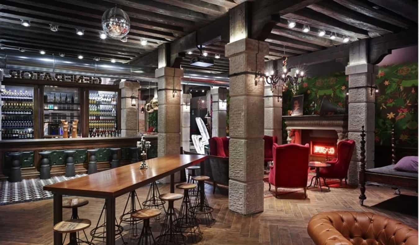 A zona geral com um bar, mesas de bar e cadeiras macias vermelhas na lareira no albergue gerador em Veneza, Itália.
