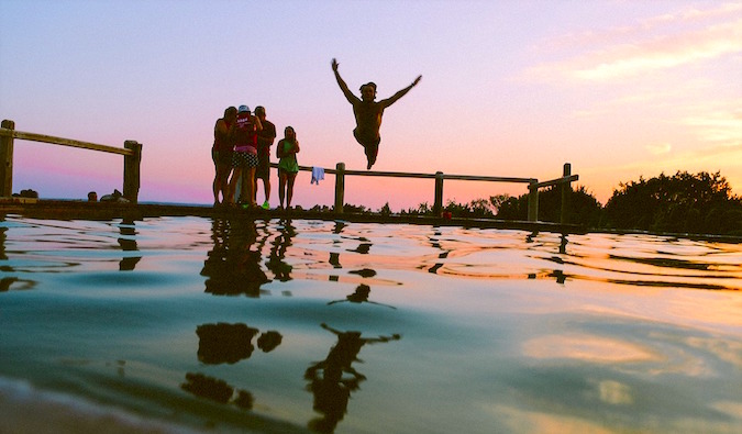 Um grupo de viajantes alegremente pula na água ao pôr do sol