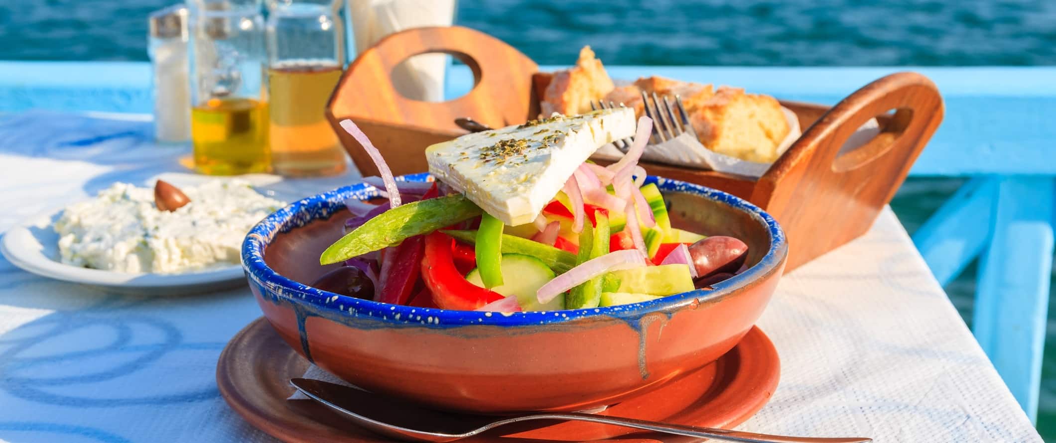 Salada grega, azeite, pão e massas à mesa perto do oceano na Grécia
