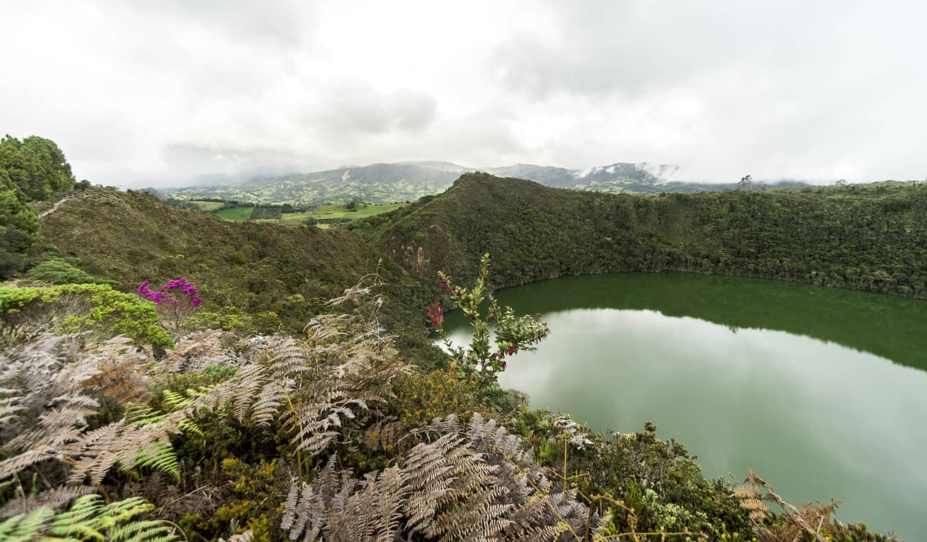 Lago de esmerald-verde Guatavita, cercado por samambaias exuberantes, ervas e colinas, na Colômbia