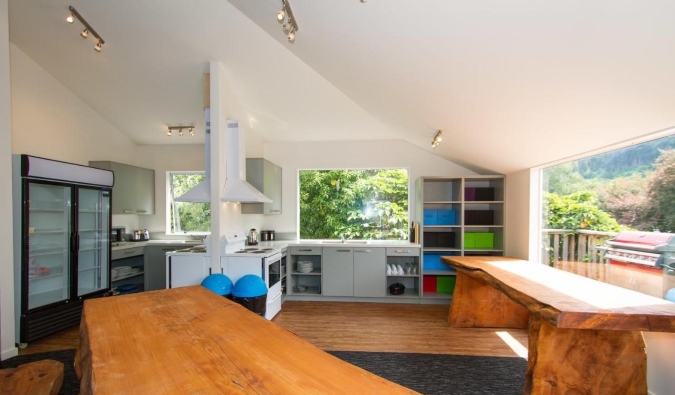 Espaçosa área comum com longas mesas de madeira, cozinha e enormes janelas no Haka Lodge em Queenstown, Nova Zelândia