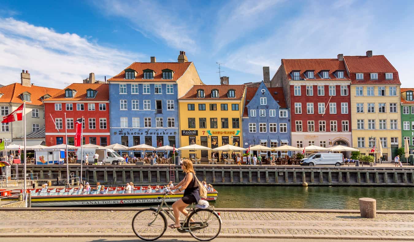 Edifícios coloridos de Copenhague ao longo da água enquanto alguém passa de bicicleta