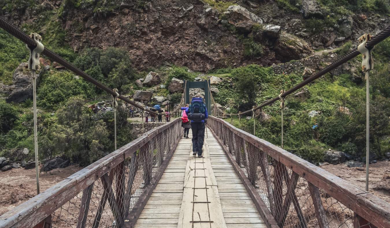 Um pedestre em uma ponte de suspensão de madeira nas cordas no início do caminho inca no Peru