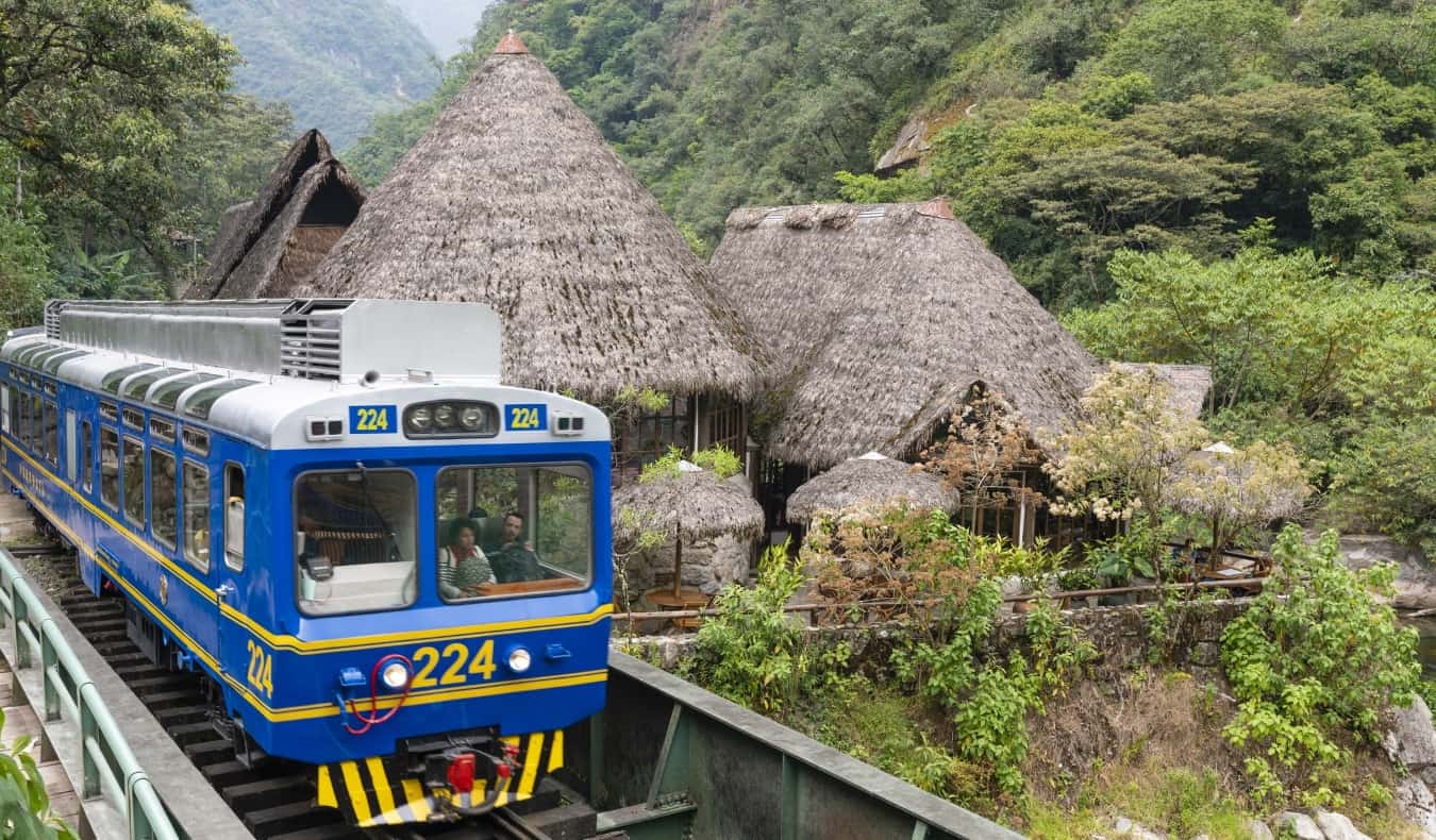 O antigo trem azul passa por casas de palha perto de Machu-Picchu no Peru < pan> medjet (revestimento de evacuação adicional)