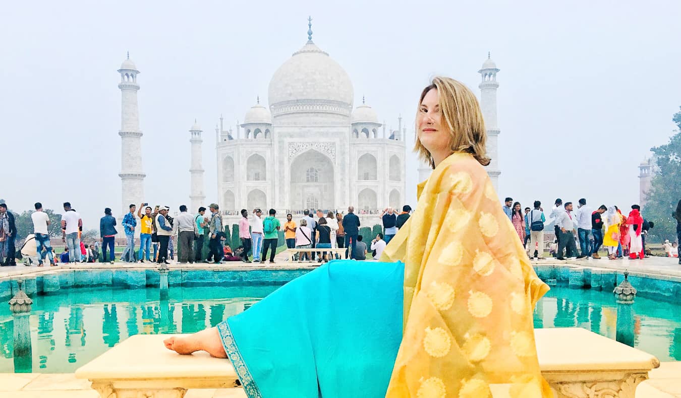 Um viajante sozinho em um sari colorido posa em frente ao Taj Mahal na Índia