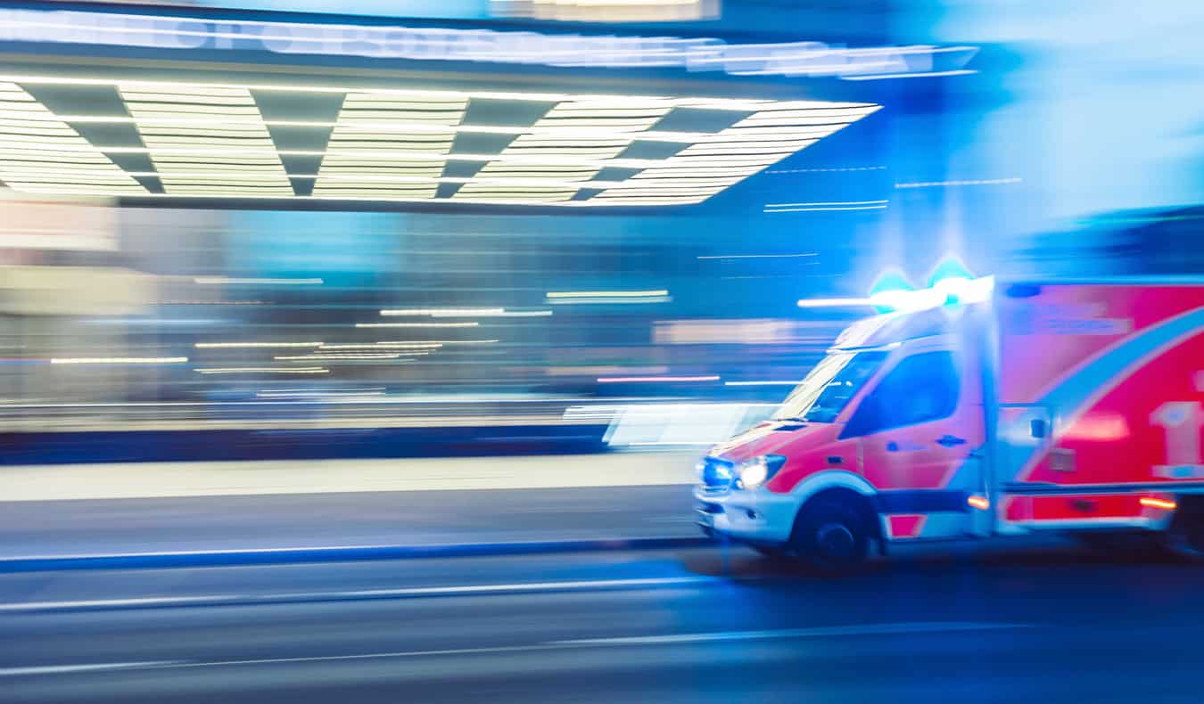Ambulância dirigindo rápido à noite com luzes piscando