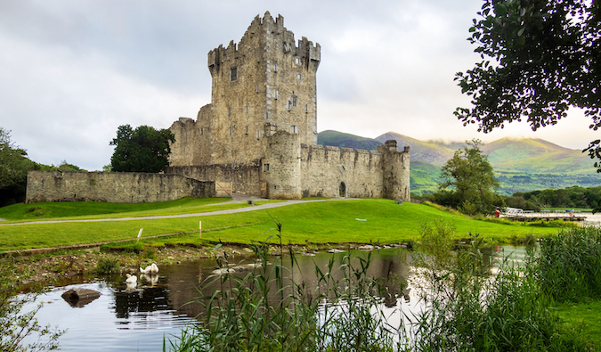 A torre de um castelo irlandês na margem de um lago tranquilo tendo como pano de fundo colinas verdes