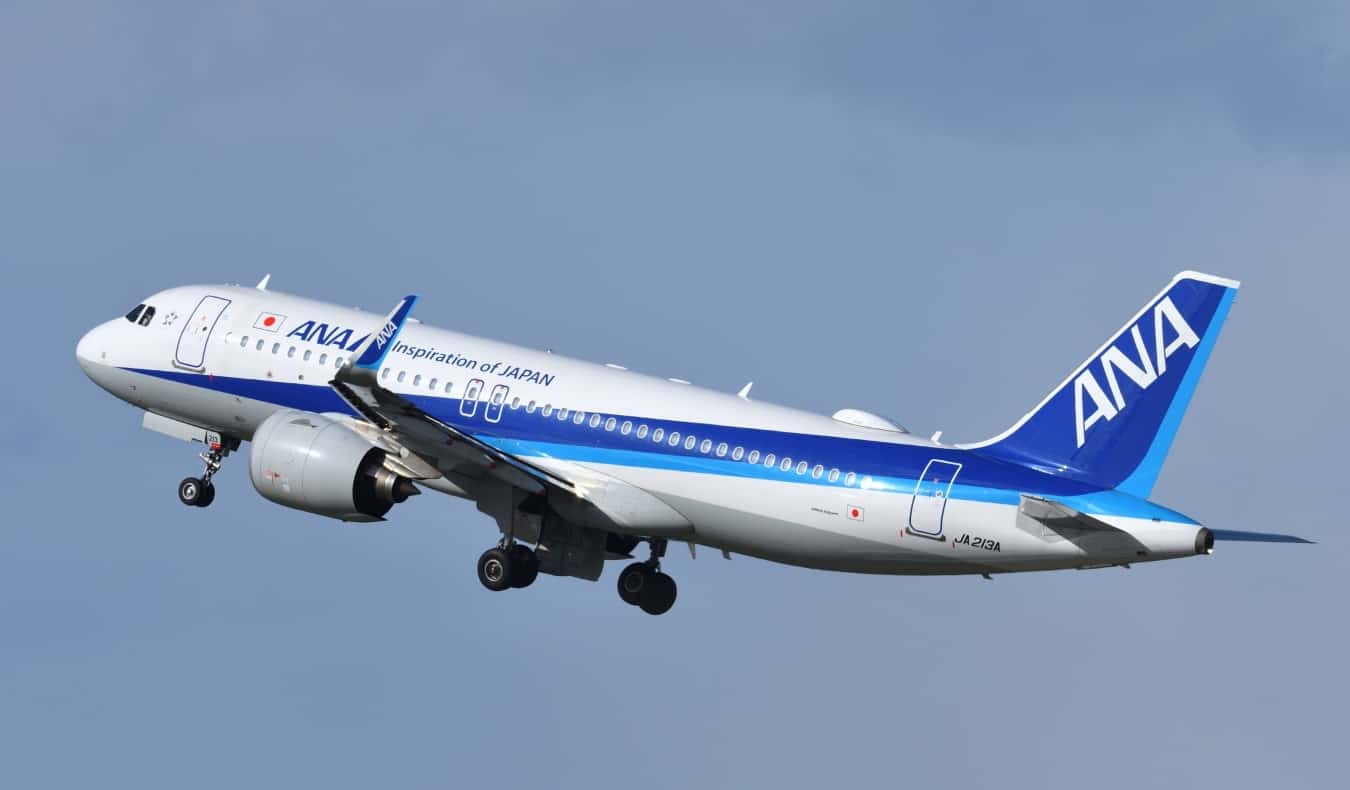 Um avião voando pelo céu com o logotipo da ANA, a maior companhia aérea japonesa.
