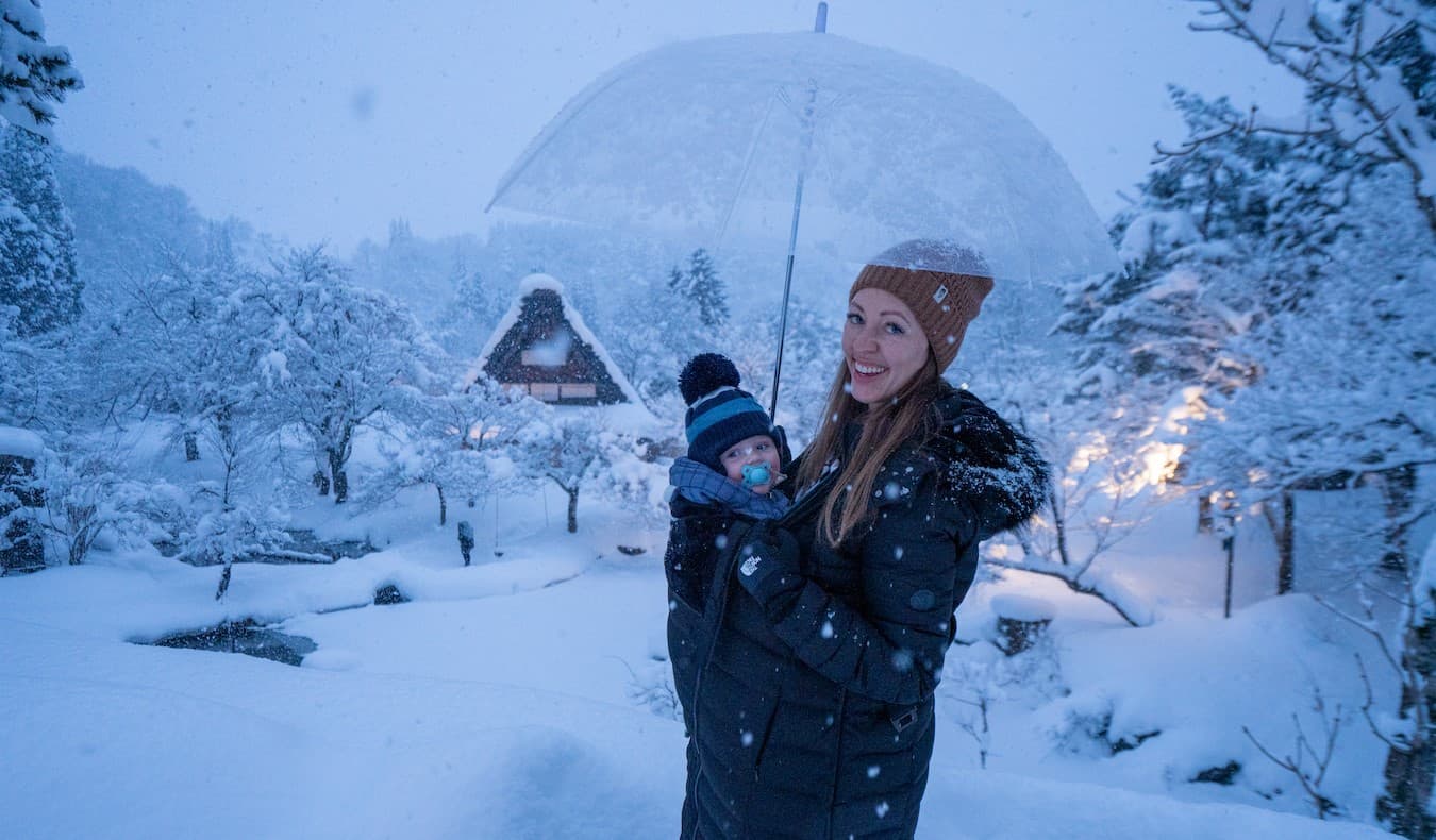 Blogger Christine Addis, de Be Mylevel Muse, com um filho infantil de transporte quando eles estão no fundo de uma paisagem nevada no Japão
