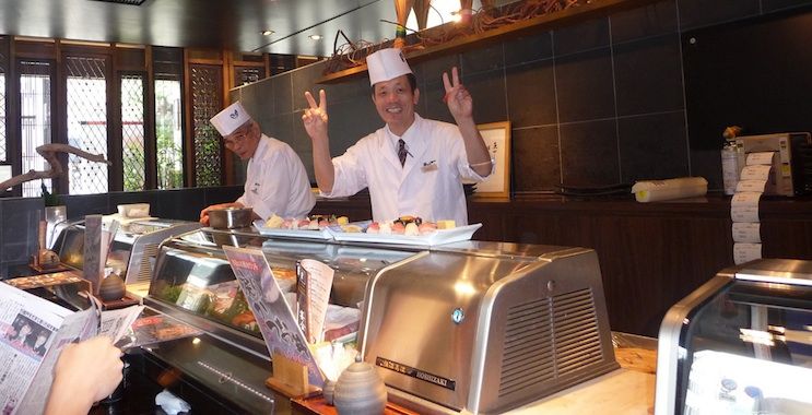 Cozinheiro japonês de sushi posa para fotografia amigável por causa do rack