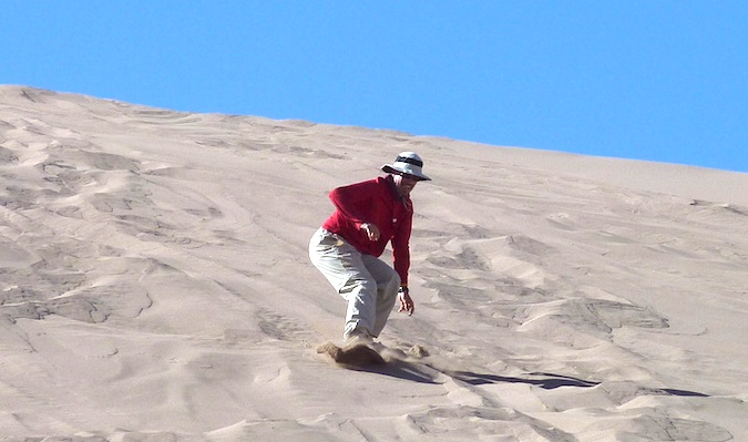 Um viajante de 50 anos desce uma duna de areia em um sandboard.