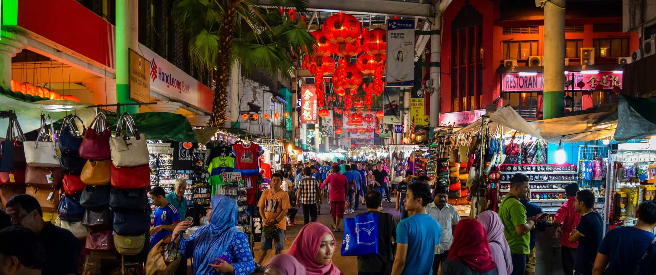 As pessoas andam ao longo de uma rua de pedestres lotadas com lojas à noite em Kuala Lumpur, Malásia