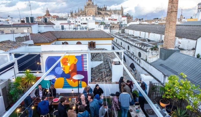 As pessoas se divertem no telhado do telhado de albergues de La Banda no Hostel com o horizonte de Sevilha, Espanha, no fundo