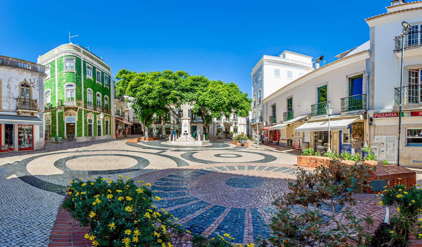 Quadrado tranquilo em Sunny Lagusha, Portugal, com muitos edifícios e árvores antigos