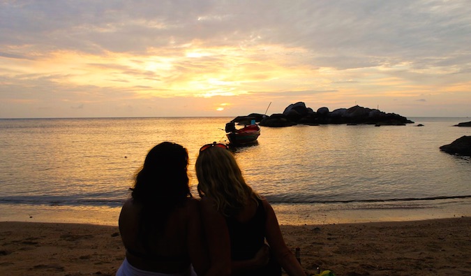 Duas mulheres juntas na praia no exterior ao pôr do sol