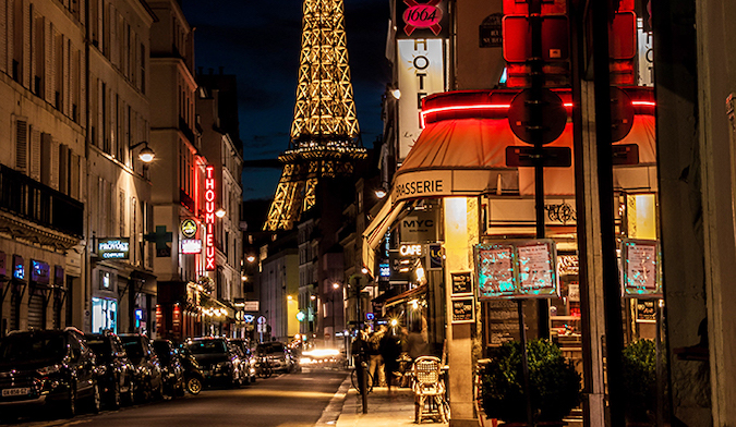 Pessoas andam em frente à torre Eiffel à noite