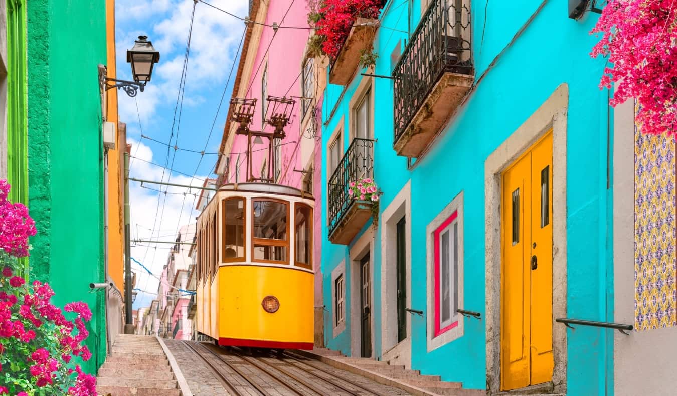 Historical Yellow Tram na rua descendo da colina ao longo da qual os edifícios e flores multifolored em varandas em Lisboa estavam alinhadas, Portigal