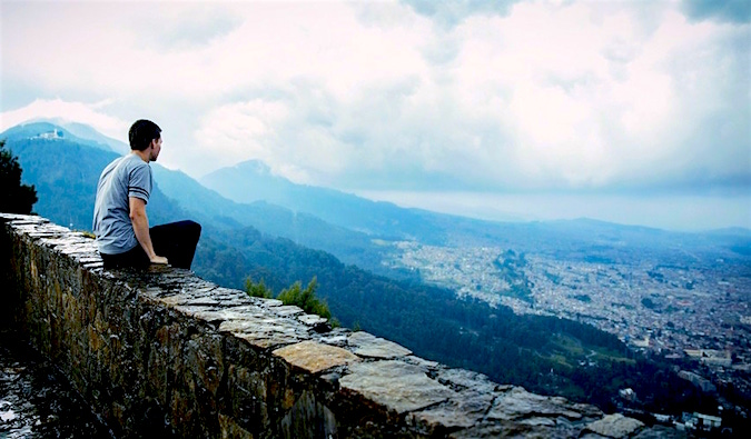 Um homem senta-se em um muro e olha para a cidade em um dia nublado