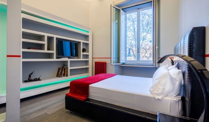 Quarto simples com cama em frente ao centro de entretenimento com prateleiras e TV no Luxury on the River Hotel em Roma, Itália