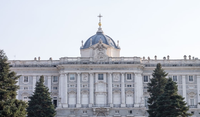 A fachada de pedra do palácio real com pinheiros na frente dele em Madri, Espanha