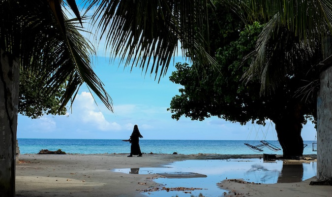 Uma mulher muçulmana local caminha pela praia nas Maldivas