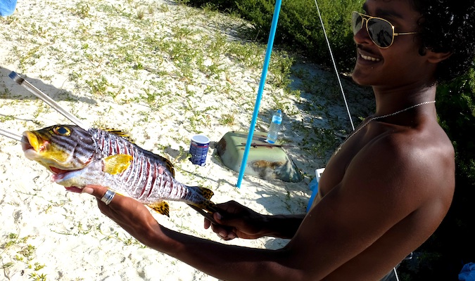 Um homem das Maldivas de óculos escuros segura um peixe grande recém-pescado.