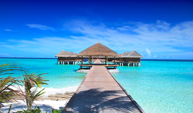 Águas azul-turquesa brilhantes das Maldivas com calçadão que leva a cabanas de palha