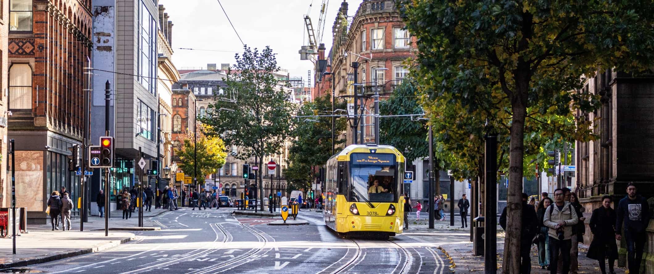 Vista das pessoas andando pela rua e passando por um bonde amarelo em Manchester, Inglaterra