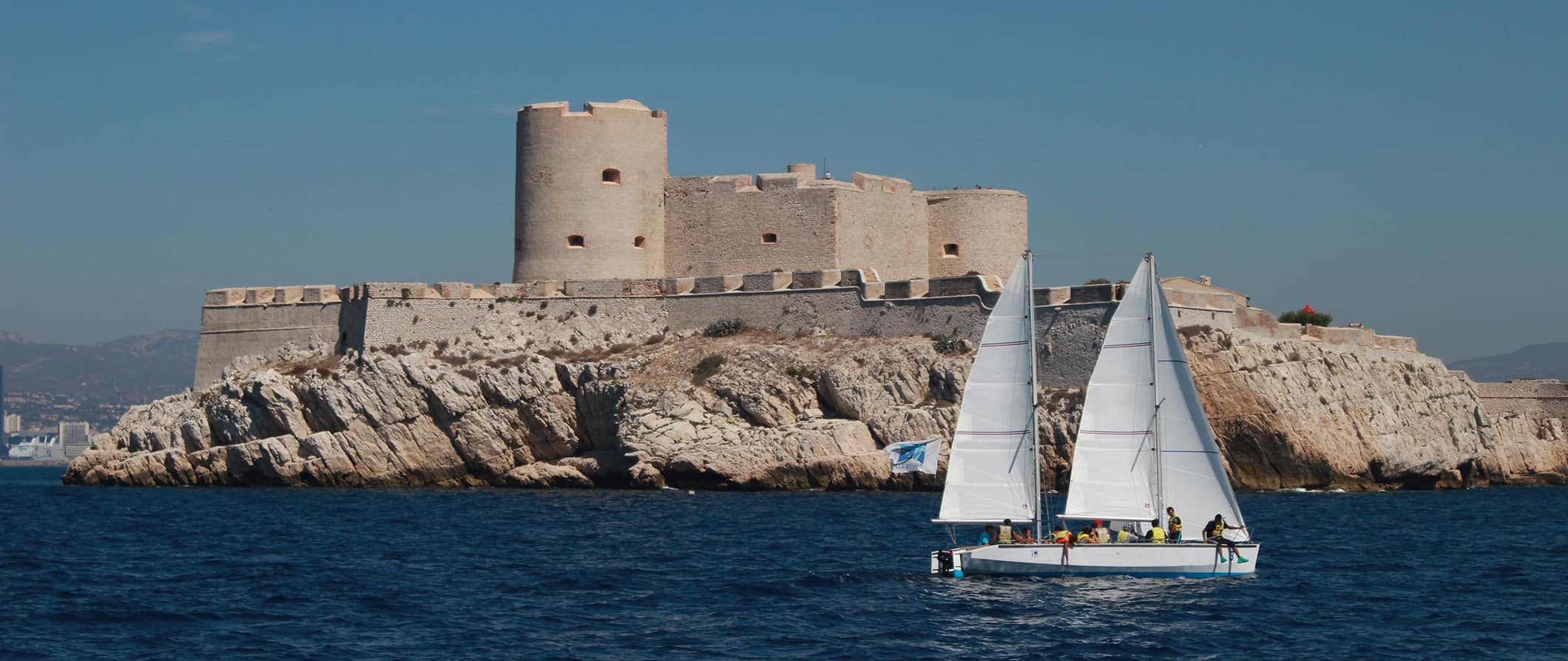 Um pequeno veleiro com passageiros navega em frente à fortaleza do Chateau d'H Se, localizado na costa de Marselha.