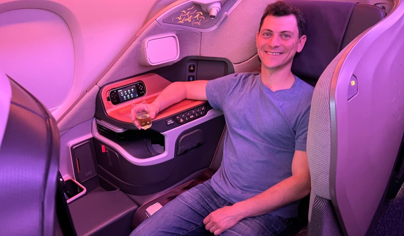 O blogueiro Nomadic Matt segura uma taça de vinho enquanto está sentado em um avião na primeira classe.