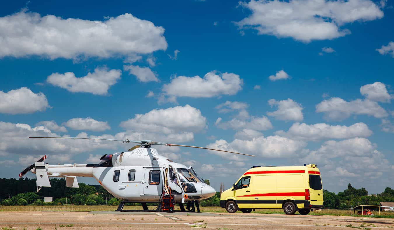 Um helicóptero estacionado em um estacionamento junto com uma pequena ambulância durante uma emergência