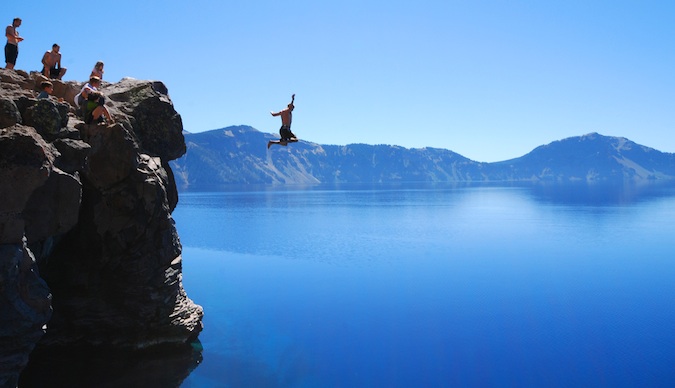 Um viajante aventureiro salta de um penhasco na sedutora água azul