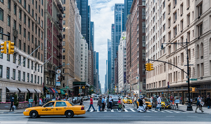 Um cruzamento animado com táxi amarelo em Nova York com muitas pessoas atravessando a rua