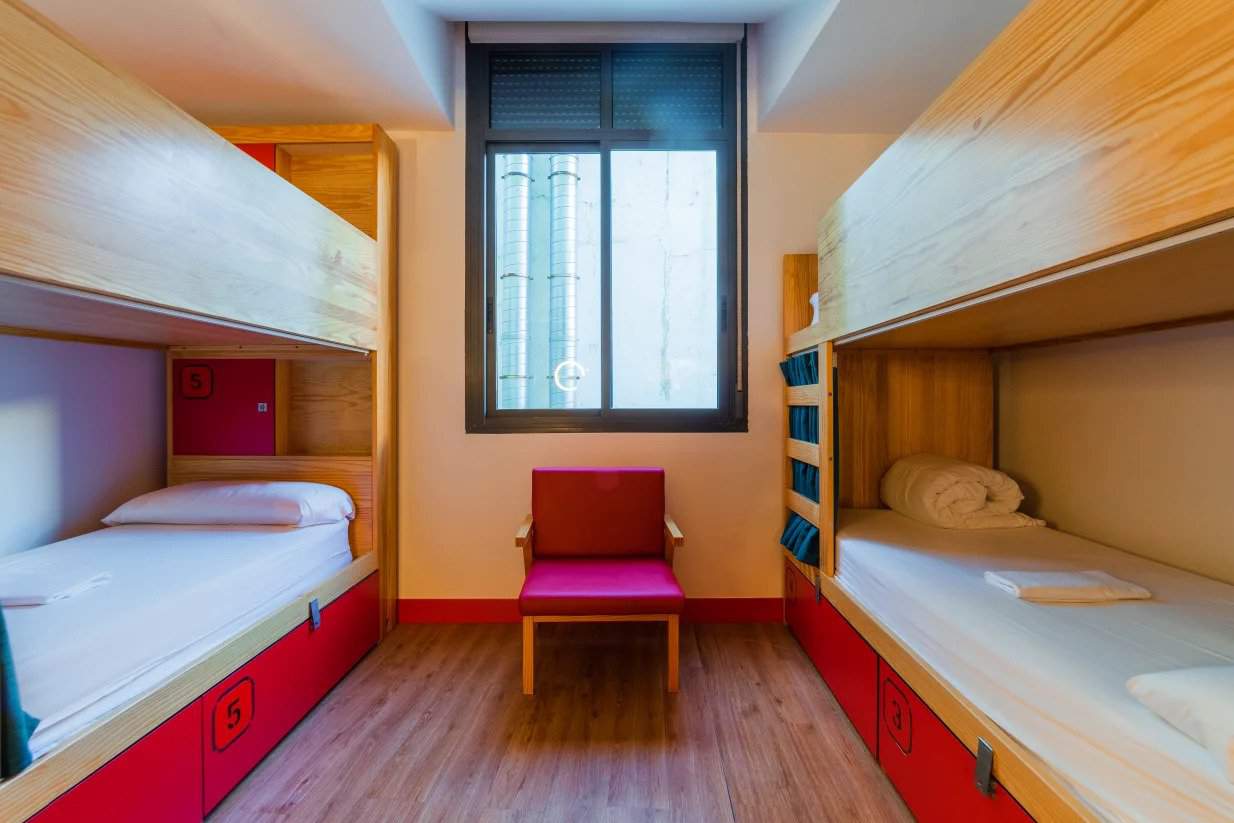 Sala comum com 2 beliches de madeira com gavetas vermelhas embaixo no Ok Hostel em Madrid, Espanha.