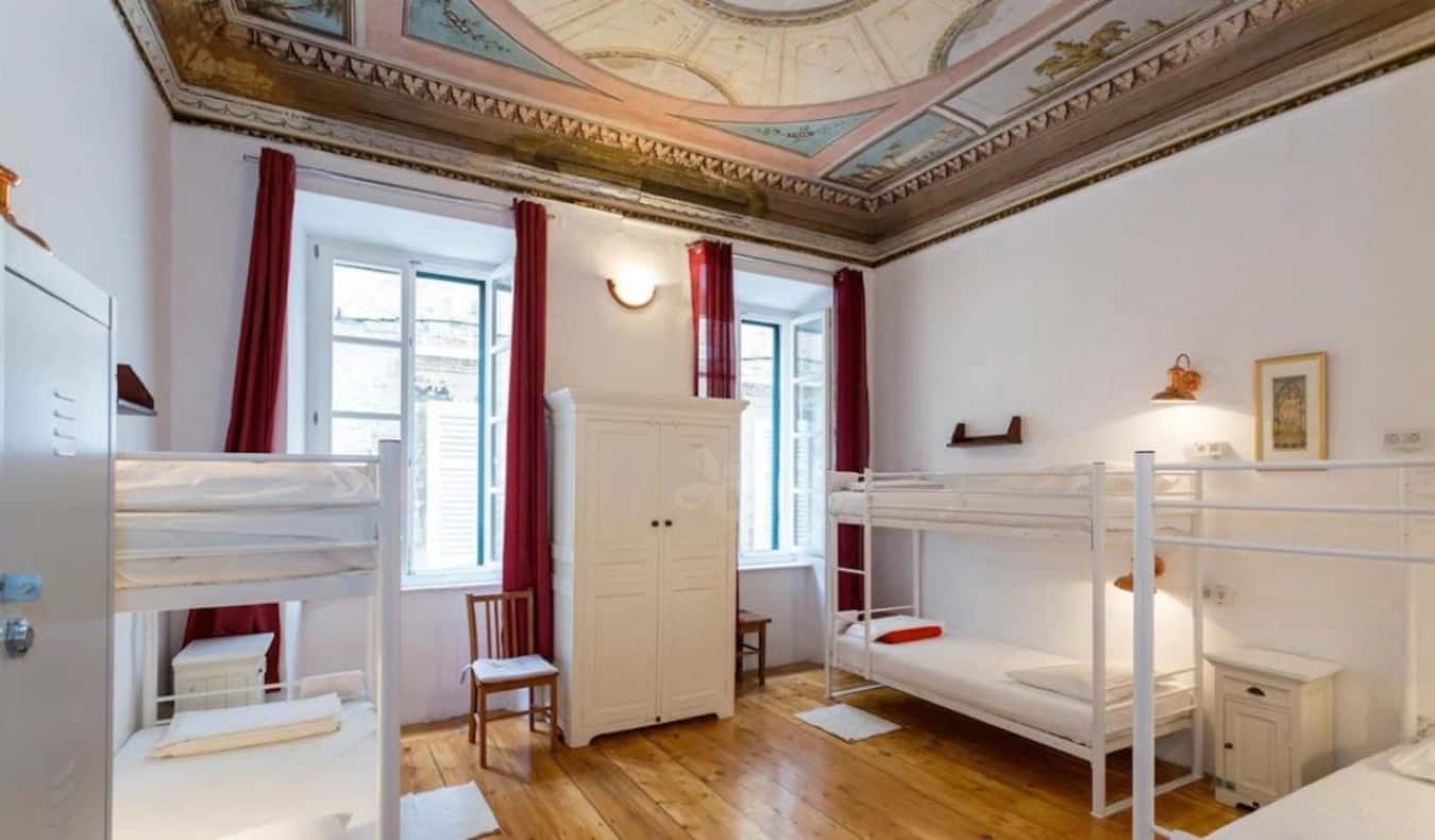 Uma sala comum com beliches, pisos de madeira e um teto ricamente decorado no albergue da cidade de Hostel em Dubrovnik, Croácia.