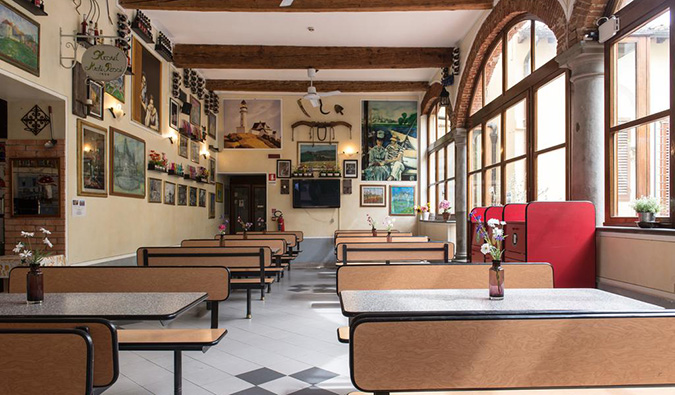 Cafeteria com muitas mesas compridas, obras de arte nas paredes e janelas em arco no Archi Rossi Hostel em Florença, Itália