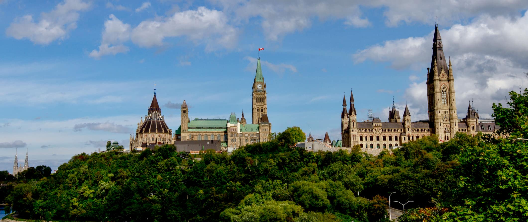 Uma vista do horizonte de Ottawa, Canadá, mostrando os edifícios do Parlamento cercados por árvores verdes exuberantes durante o verão.