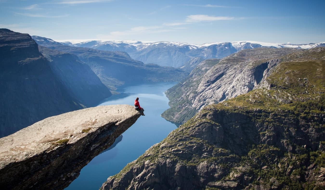 Um homem sent a-se em um penhasco de Troltung sobre o fiorde na Noruega