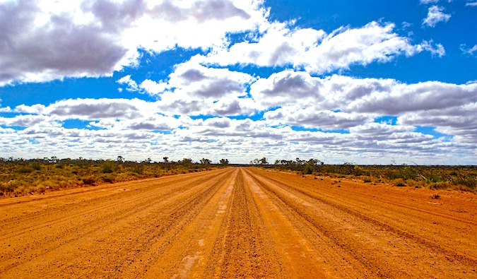 Uma estrada empoeirada vazia no interior australiano em um dia ensolarado brilhante.