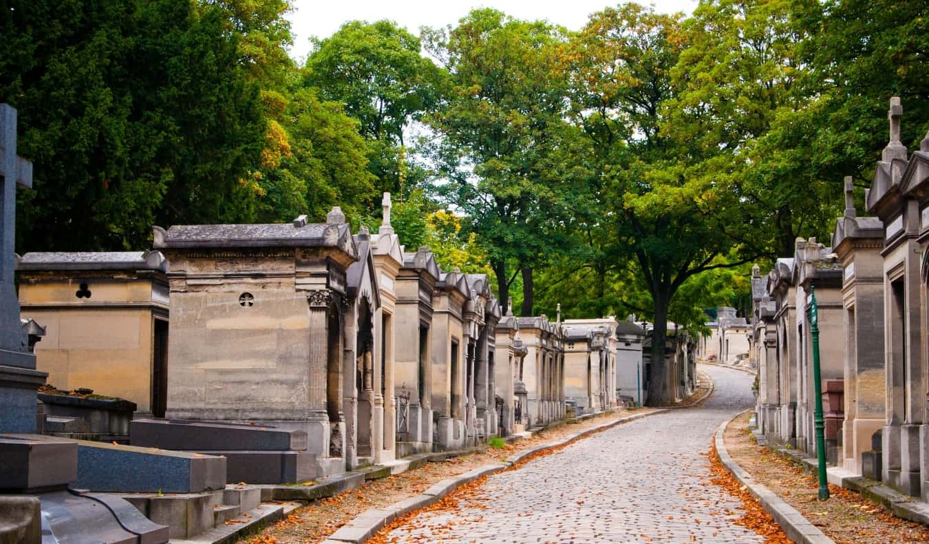 Mausoléus alinham-se em um caminho de paralelepípedos repleto de folhas de laranja no Cemitério Père Lachaise, em Paris, França