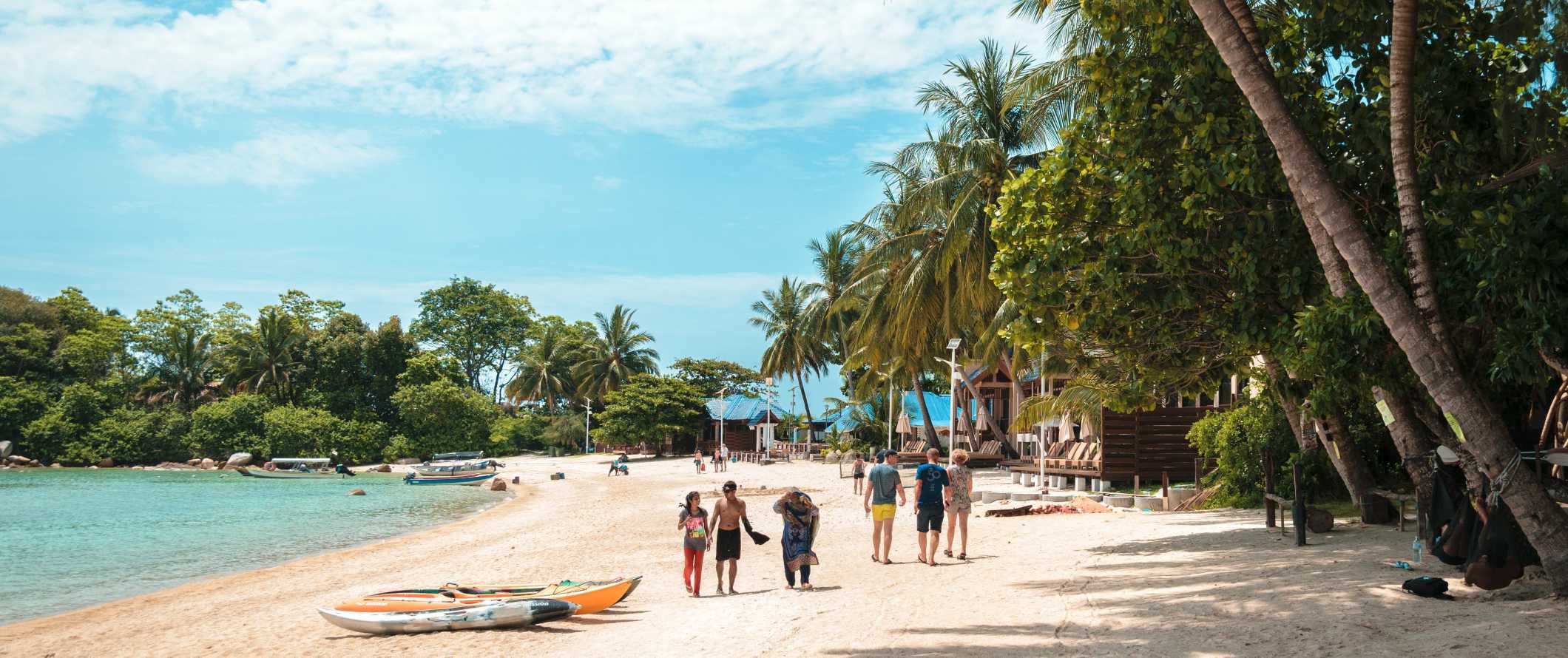 Pessoas caminham ao longo de uma praia com águas claras e palmeiras exuberantes nas Ilhas Perhentian, Malásia