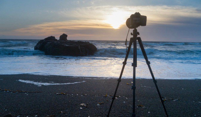 O tripé e a câmera estão instalados na praia no exterior durante um pôr do sol relaxante