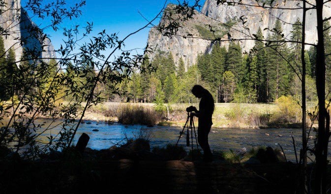 Um fotógrafo profissional está se preparando para atirar na natureza no cenário de um céu azul