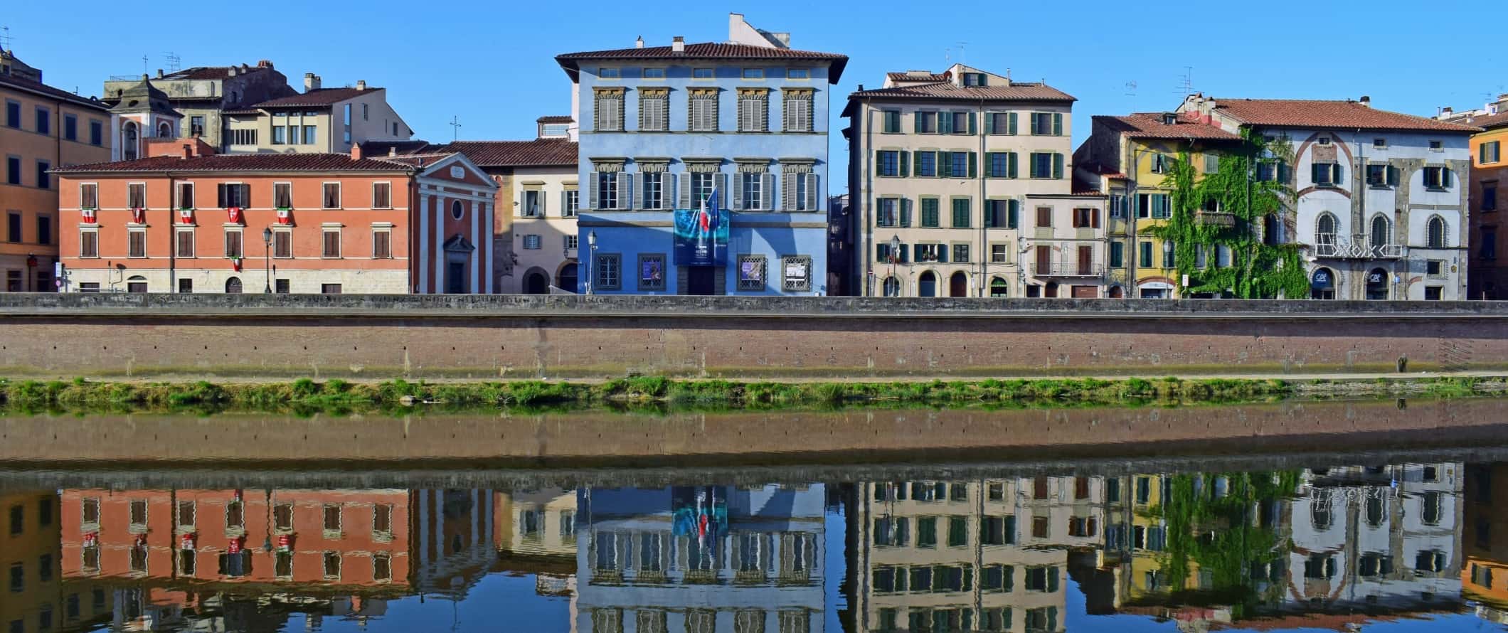Edifícios históricos pintados em cores vivas, incluindo o centro de artes azul Palazzo Blu, alinham-se às margens do rio Arno, em Pisa, Itália.