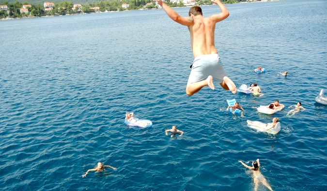 Uma pessoa pula na água de um penhasco, viajando pelo mundo