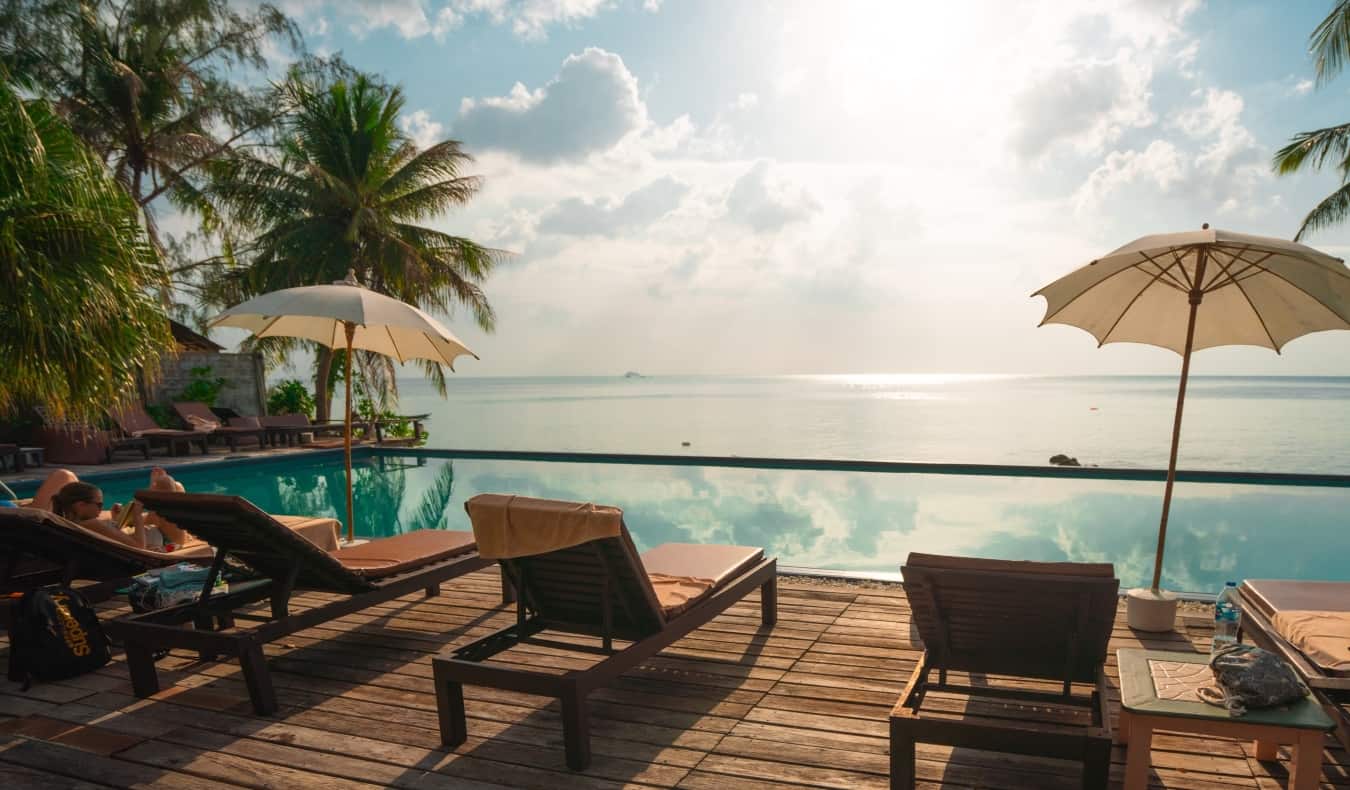 Espreguiçadeiras à beira de uma piscina infinita cercada por palmeiras em um resort de luxo.