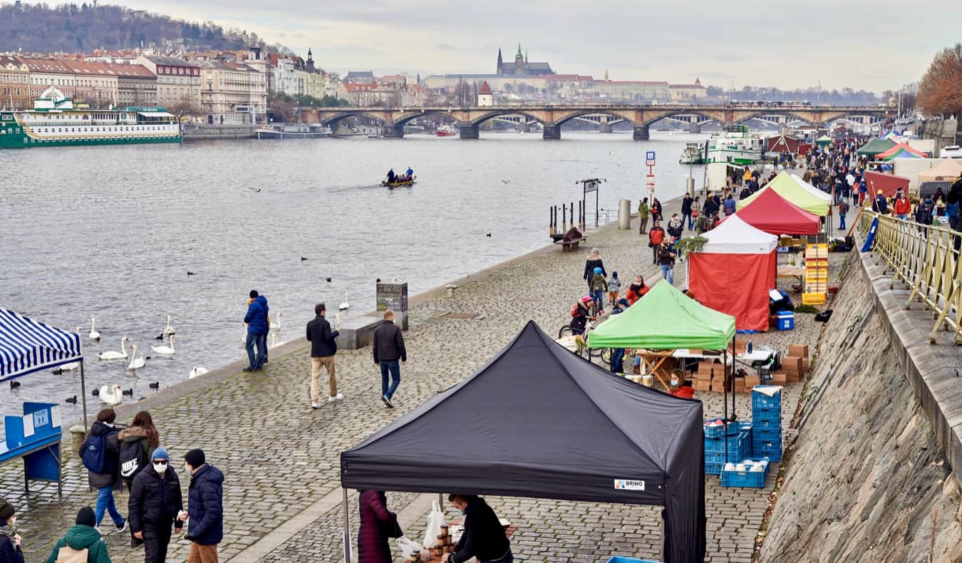 As pessoas andam perto dos quiosques ao longo do rio em Praga, a República Tcheca