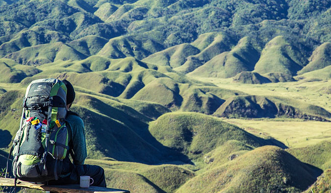 Um turista solitário sent a-se em uma cordilheira e desfruta de uma bela vista da paisagem aberta na frente